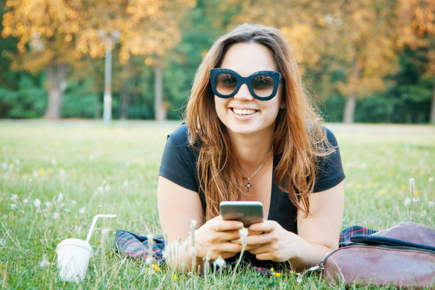 улыбающаяся девушка лежит на траве - glasses grass women lying on front стоковые фото и изображения