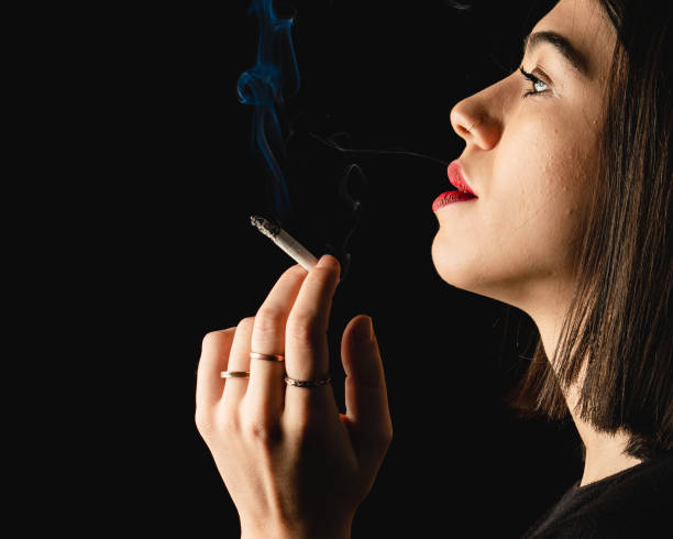 istock Low key close-up young woman smoking cigarette on black background. 1223882777
