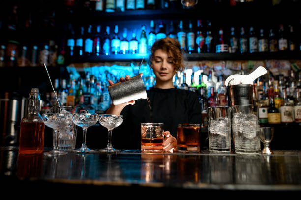 Young lady at bar pours cocktail into glass. Young lady at bar pours cocktail into glass. Different bar equipment stand on bar counter. bartender photos stock pictures, royalty-free photos & images