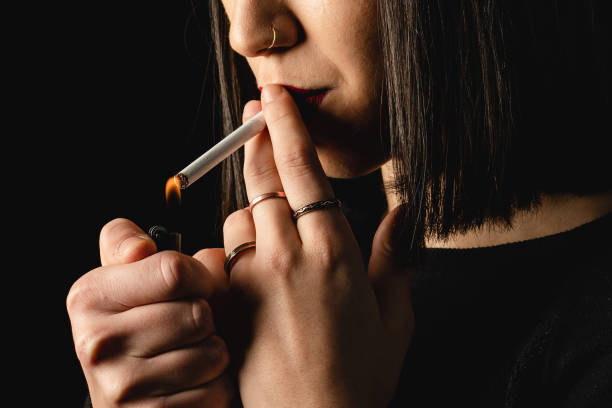 istock Low key close-up young woman smoking cigarette on black background 1223887686