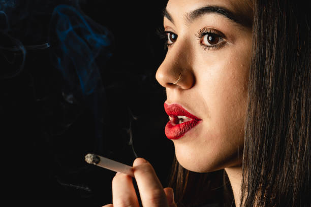 Low key close-up young woman smoking cigarette on black background stock photo