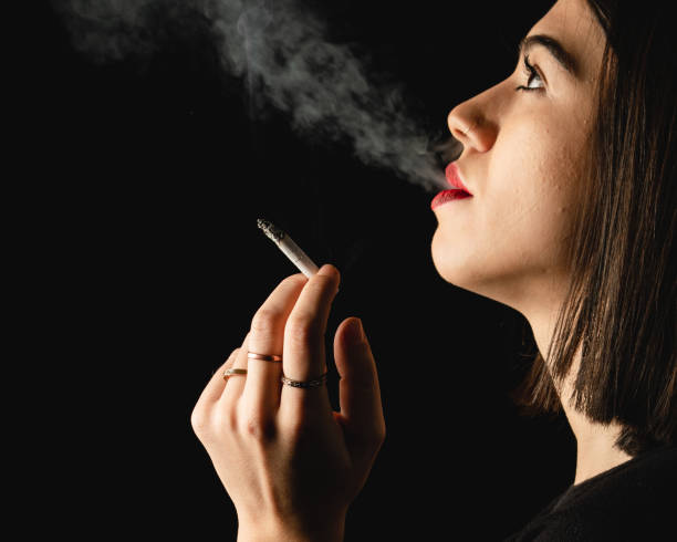 istock Low key close-up young woman smoking cigarette on black background 1223887777
