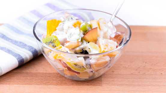 Cup with fruit salad with greek yogurt on the table close-up, top view - banana, grape, kiwi, apples, orange