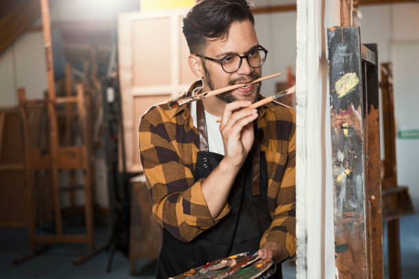 istock Young painter holding a color palette and paintbrush in his art studio 1223889085