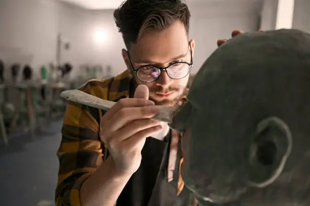 Photo of Young man with eyeglasses sculpting head out of clay