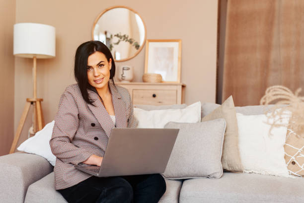 istock Young beautiful woman using a laptop computer at home, sitting on the sofa, working home 1223891978