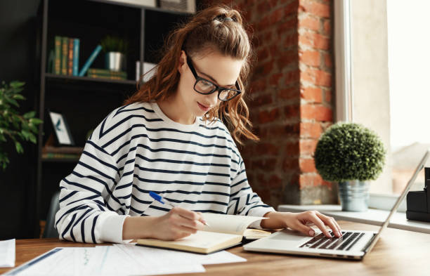 istock Happy millennial woman taking notes in notepad while working at laptop in comfortable loft office 1223894041
