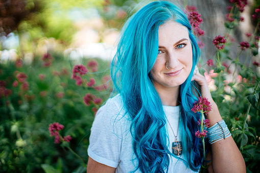 Unique Spunky Fashionable Young Woman 20-Something Girl with Fun Cute Teal Blue Green Dyed Hair Posing for a Portrait with Pink Flowers Outdoors in the Summer