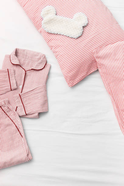 istock Pajamas sleeping outfit, fluffy sleeping eye mask, pillow and blanket on white bed sheet with copy space. Top view. Flat lay. 1223909622