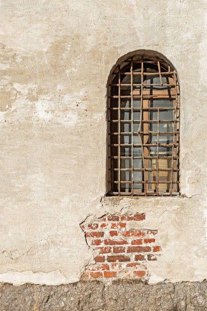 istock Window  with the broken  bars on light concrete wall. Wall of old Tower. Historical Old building. 1223913516