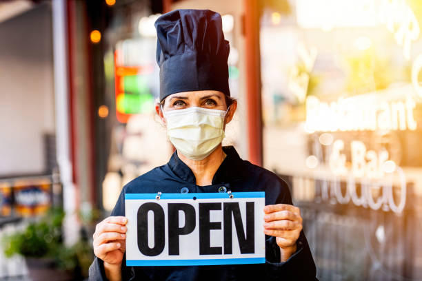 오픈 사인을 들고 마스크를 쓰고 포즈를 취하는 여성 셰프 레스토랑 주인 - owner restaurant business worried 뉴스 사진 이미지