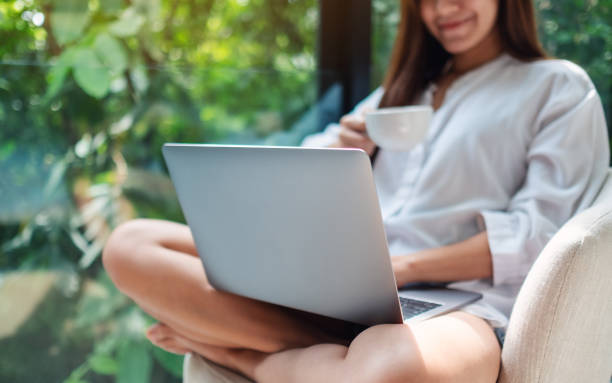 istock a beautiful woman working and typing on laptop computer while drinking coffee and sitting on a white armchair at home with green nature background 1223920267