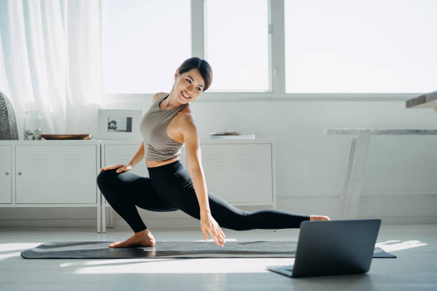 joven asiática haciendo clase de yoga en línea con computadora portátil en la sala de estar en casa por la mañana - stretching yoga zen like beauty fotografías e imágenes de stock