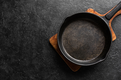 Empty cast iron frying pan for cooking on black background, top view, copy space. Cooking concept background with black pan.