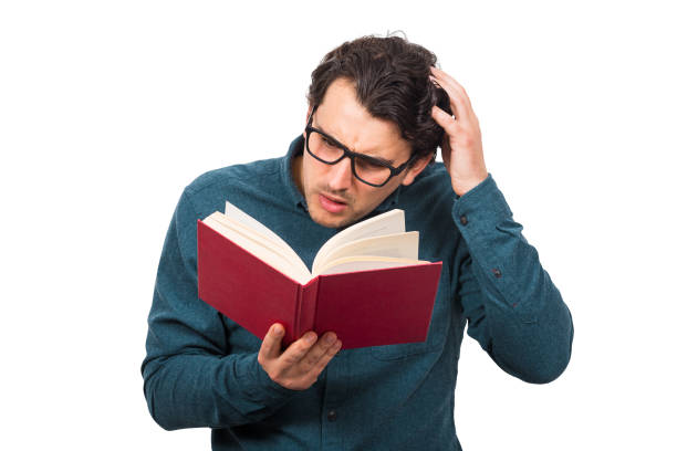 istock Puzzled man reading a book, scratching his head, isolated on white background. Student or professor wears eyeglasses looking confused in a textbook. Education concept, studying and learning home. 1223935416