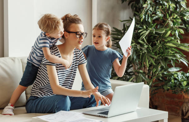 Stressed woman with kids working from home Tired young mother sitting on sofa and working with laptop and documents while little kids having fun and making noise exhaustion photos stock pictures, royalty-free photos & images