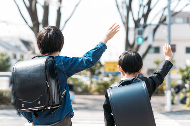 gli studenti delle scuole superiori giapponesi e i bambini di prima elementare alzano la mano a un incrocio - randoseru foto e immagini stock