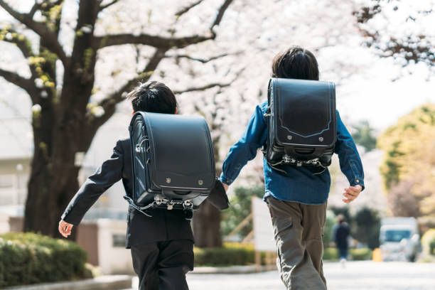 japanische obergrundschüler und erstklässler heben an einer kreuzung die hände - randoseru ranzen stock-fotos und bilder