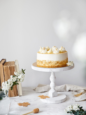 Homemade Russian layered cake with honey Medovik with cream and merengue on the top. White flowers, autumn leaves, old books nearby on the white table at white background