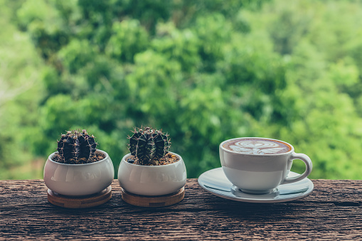 Latte art coffee cup with cactus pots on wooden table