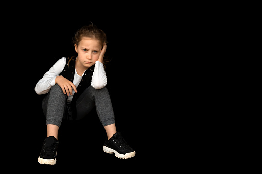 Sad blonde 9 years old, little schoolgirl, serious girl isolated on black background, copy space.