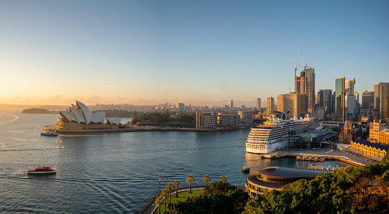 Sydney, Australia - August 05, 2019: The spectacular cityscape of Sydney at dawn. Across the waters of Sydney Harbour we see the iconic form of the city's Opera House and the Harbour beyond. The cruise ship Carnival Spirit is moored tied up at the Overseas Terminal.