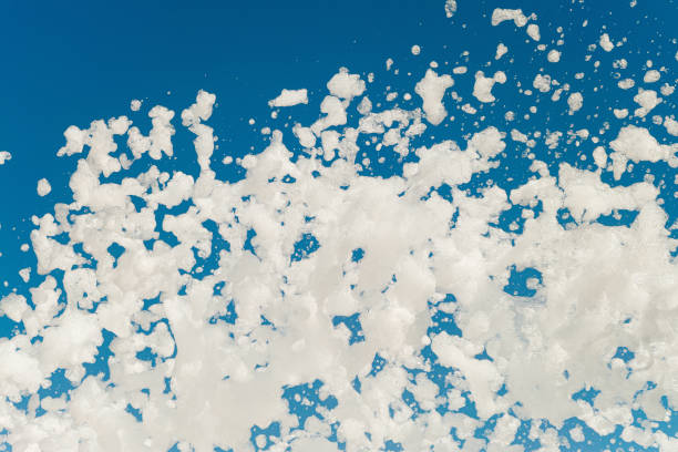 Foamy disco party. White airy foam on a blue sky background blowing from lather maker gun.