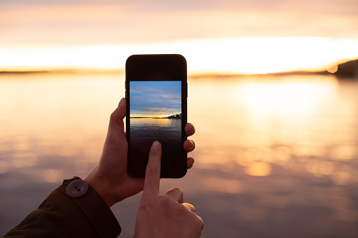 Female photographing sunset scenery with smart phone camera