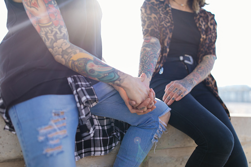 Close up of alternative hipster lesbian couple sitting together, holding hands outdoors
