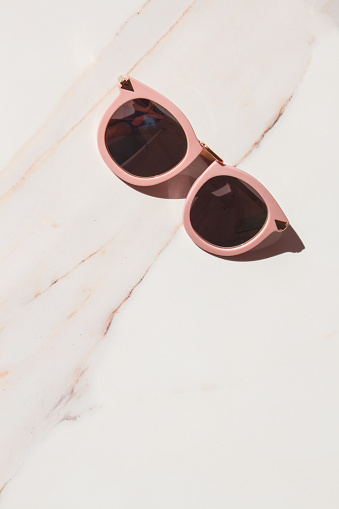 Fashionable female pastel glasses on white marble with hard light and shadows. minimal concept. Blogger concept.