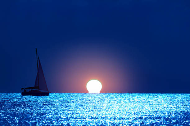 Hình bóng của một chiếc thuyền buồm trên biển mở với ánh trăng lấp lấp ngôi.