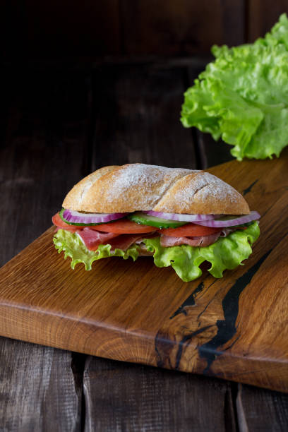istock Long subway sandwich with italian meat on wood board 1223968563