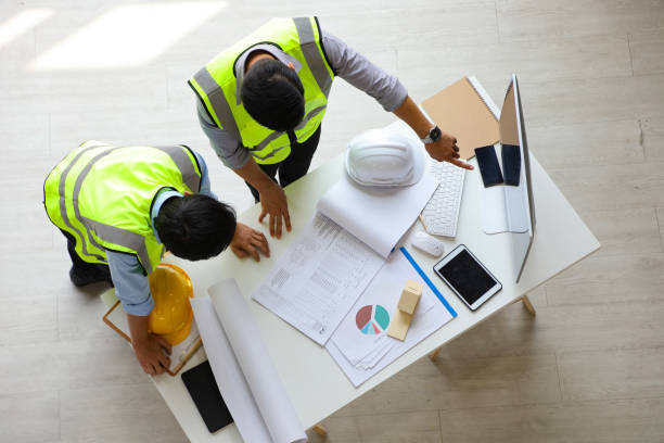 istock Two Asian engineers wearing safety equipment while discussing over the future expanding business plan with blueprint of the factory inside the warehouse from the top view 1223971521