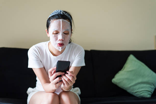 istock Asian woman using phone while applying cosmetic face mask at home 1223980322