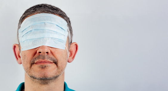 isolated blindfolded man with surgical mask over the eyes and bare mouth and nose