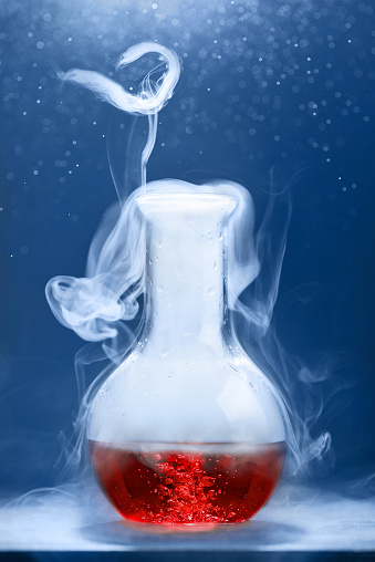 Vertical shot of glass flask with a red liquid is steaming on blue background.