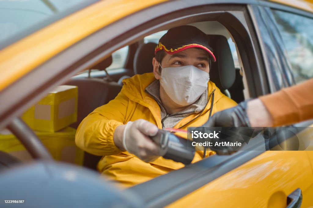 Contactless payment for taxi during an illness epidemic. Taxi driver and his passenger wearing protective masks and gloves Man protected with rubber gloves paying for taxi using credit card. Delivering Stock Photo