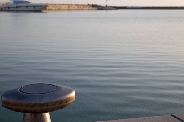 Blue mooring bollard on a concrete dock with calm water reflecting the golden light of sunset in the background.