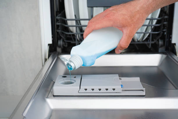 Hand filling dishwasher with blue liquid into the dishwasher box. stock photo
