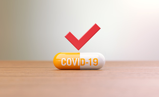 COVID-19 written yellow pill  sitting on brown wood surface in front of abstract defocused background. Horizontal composition with selective focus and copy space. Front view. COVID-19 treatment concept.