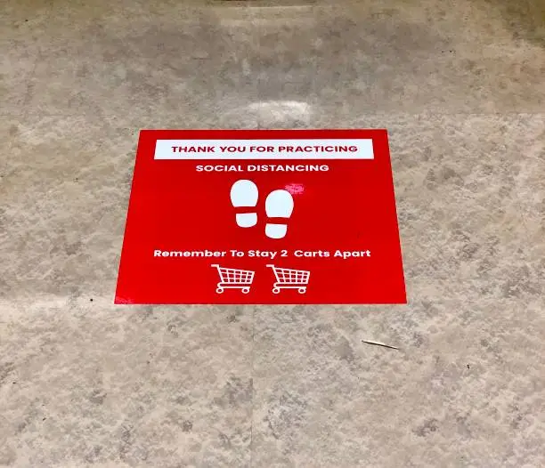 Sticker on the floor of a retail grocery store requesting that customers practice social distancing and stay 2 carts apart