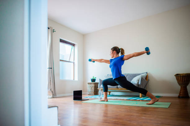 istock Back side view Young girl doing online exercise session at home with dumbbells arms stretched out 1223999795