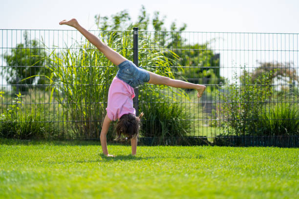 5 year old girl exercising on meadow in private garden practicing cart wheels during long vacation in summer