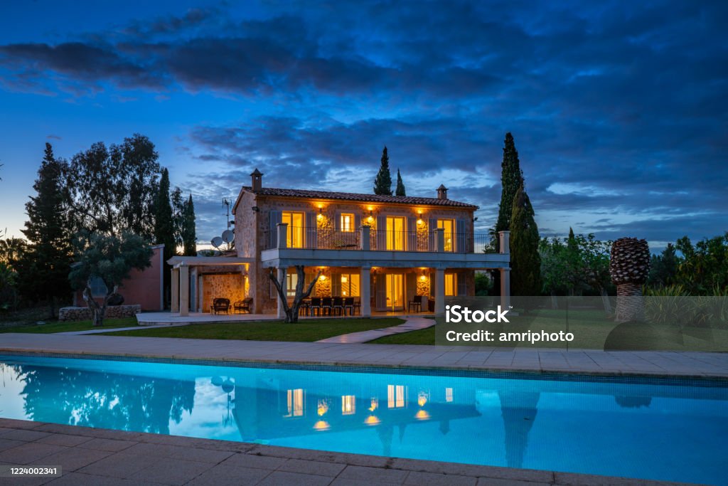 beautiful spanish finca illuminated in the evening typical spanish finca, house with huge garden and swimming pool with reflections on island of Majorca on cloudy evening Real Estate Stock Photo