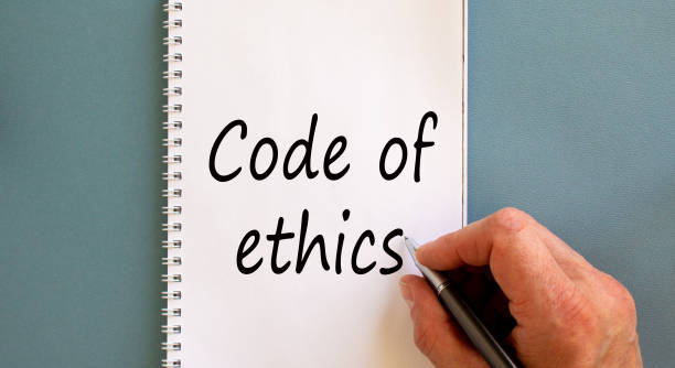 istock Male hand writing 'Code of ethics' on white note, isolated on blue background. 1224003119