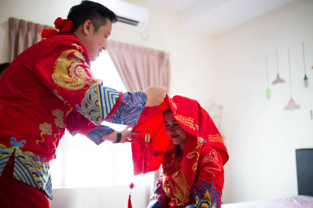 una pareja de asia teniendo su ceremonia de boda tradicional china. novio levantando velo nupcial para besar a la novia hermosa. - asian culture dragon textile symbol fotografías e imágenes de stock