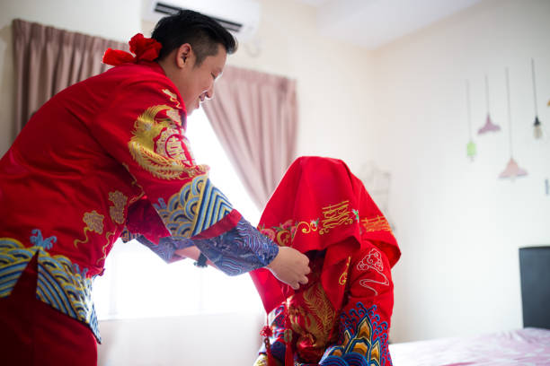 una coppia asiatica che ha la cerimonia nuziale tradizionale cinese. groom solleva il velo nuziale per baciare la bella sposa. - asian culture dragon textile symbol foto e immagini stock