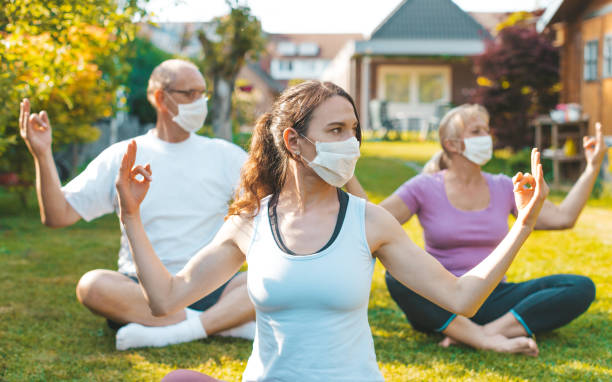 Multigenerational group of people making yoga exercises outdoors wearing medical protective masks Concept of life during or after quarantine, coronavirus protection measures yoga class photos stock pictures, royalty-free photos & images