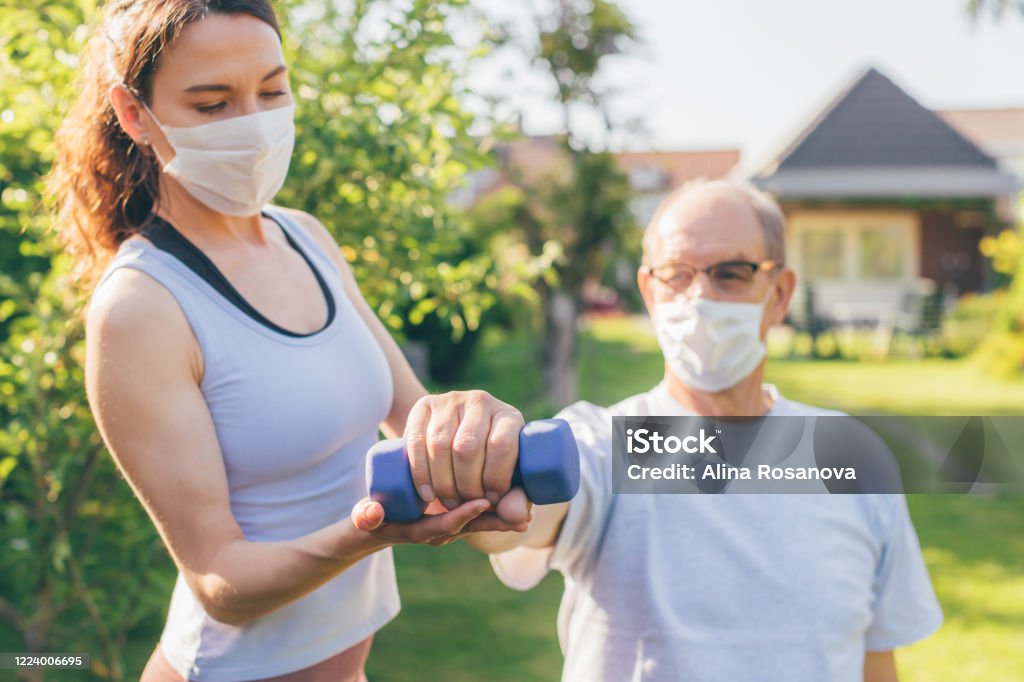 Senior man making physiotherapy session with young doctor (woman) Concept of physical therapy during or after covid-19 outbreak - focus on the hand with dumbbell Physical Therapy Stock Photo