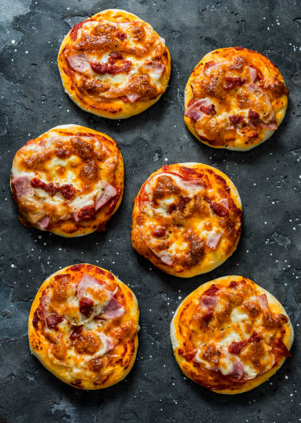 istock Mini ham, tomato sauce, mozzarella, sun dried tomatoes pizza on a dark background, top view. Delicious breakfast, snack, tapas 1224009672